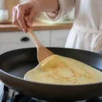 Yapışmaz tavada ince krep pişirirken spatulayla kenarını kaldıran kişi